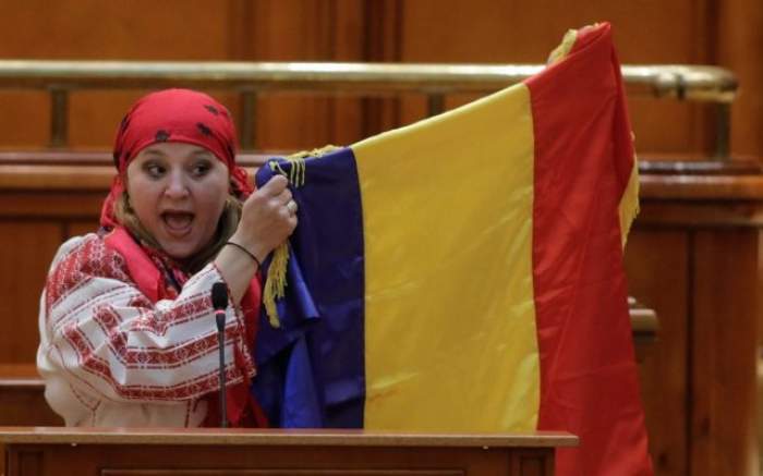 Diana Șoșoacă ține un discurs în Parlamentul României, în timp ce poartă haine tradiționale și drapelul țării ridicat