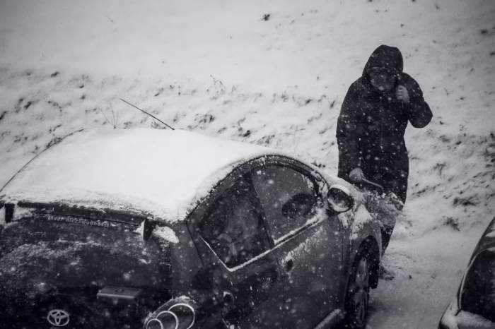 persoană care dă zăpada de pe mașină