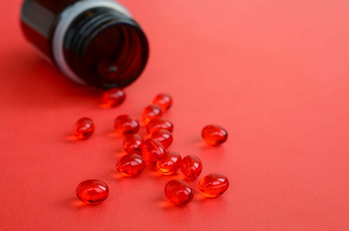 O mulțime de tablete roșii transparente au fost împrăștiate dintr-un borcan mic de sticlă maro pe o suprafață roșie