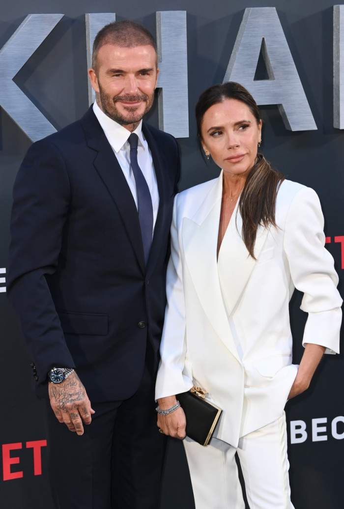 David Beckham în costum negru și soția lui, Victoria Beckham, îmbrăcată în alb