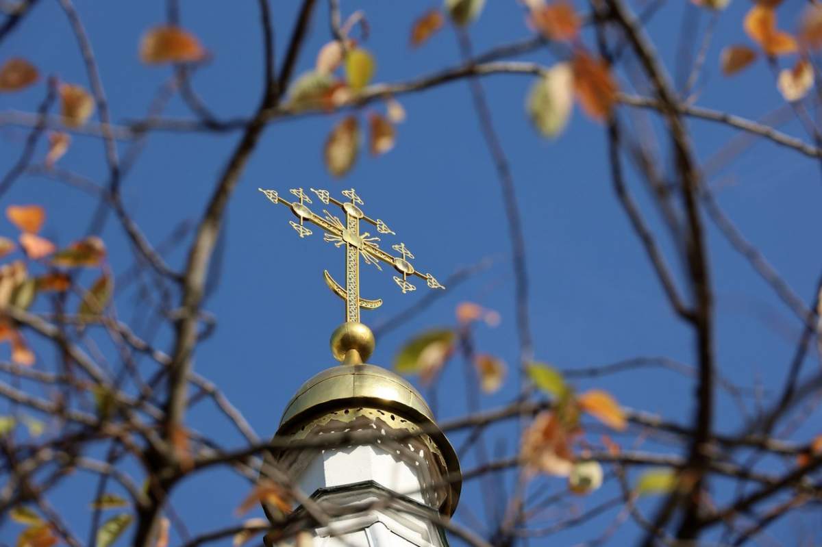 Vedere prin copacul de toamnă la templul Bisericii Ortodoxe. Clopotniță veche cu cruce de aur într-o pădure