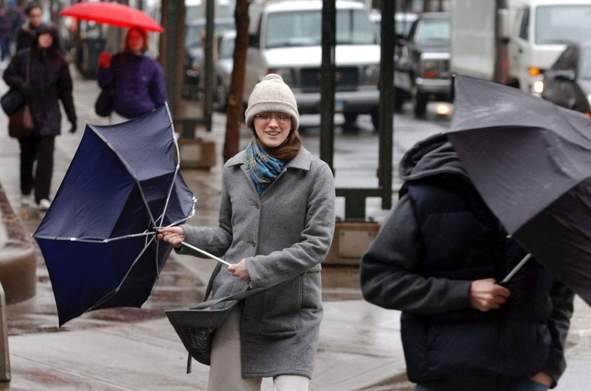 Oameni pe stradă cu umbrele în vânt