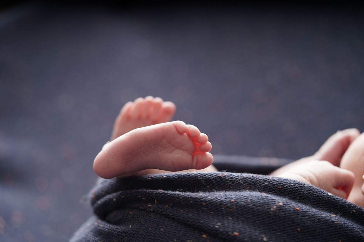 Bebeluș mic desculț încrucișat pe o pătură de fundal bleumarin.