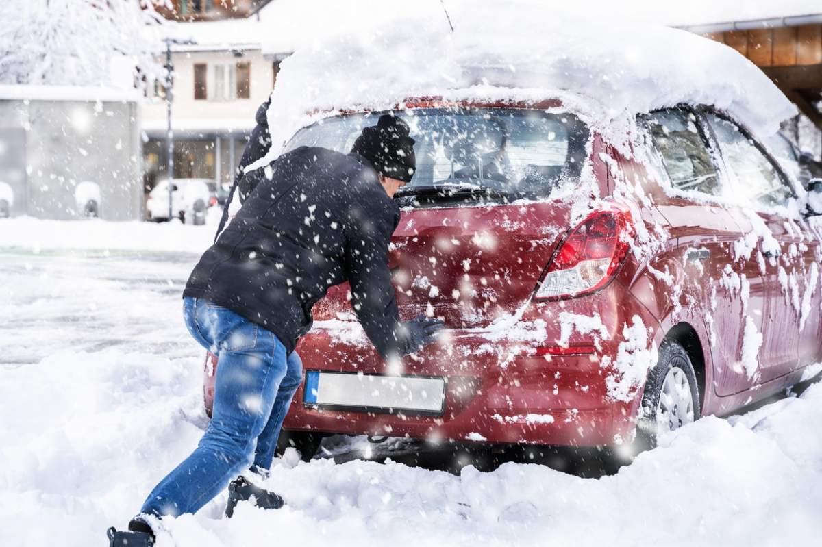 Bărbat împingând o mașină blocată în zăpadă