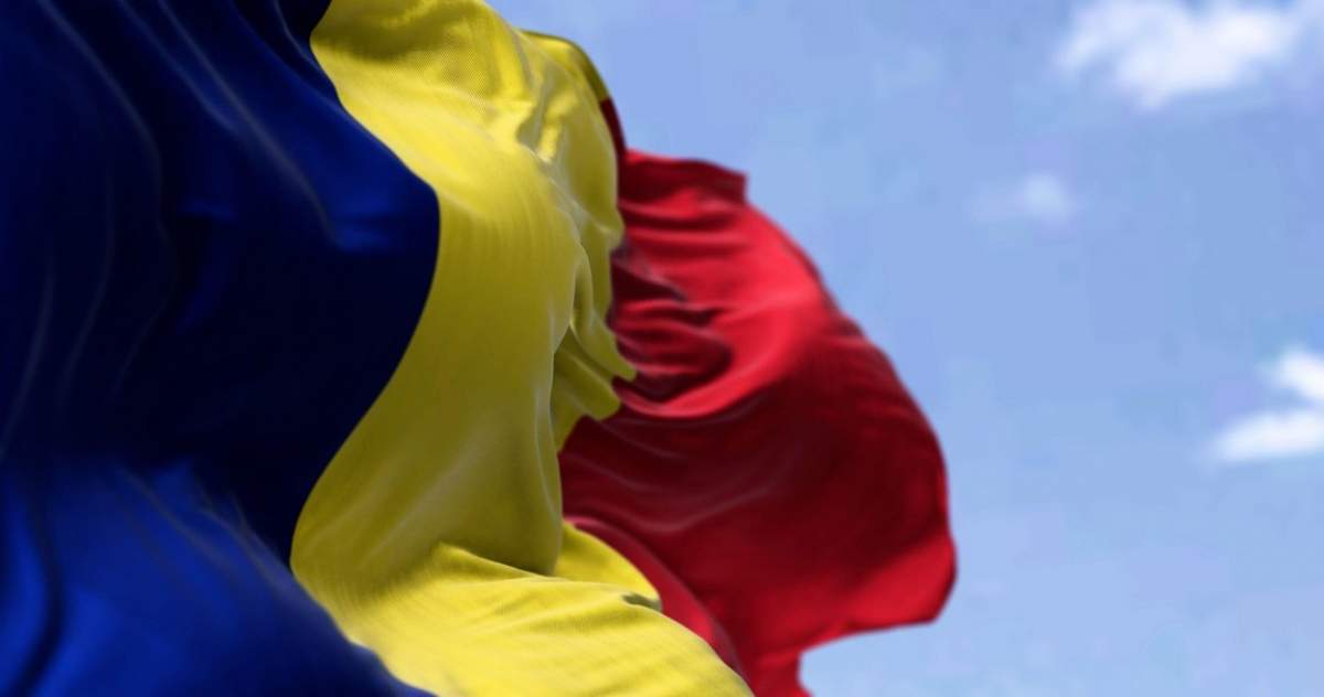 Detaliu al drapelului național al României fluturând în vânt într-o zi senină.