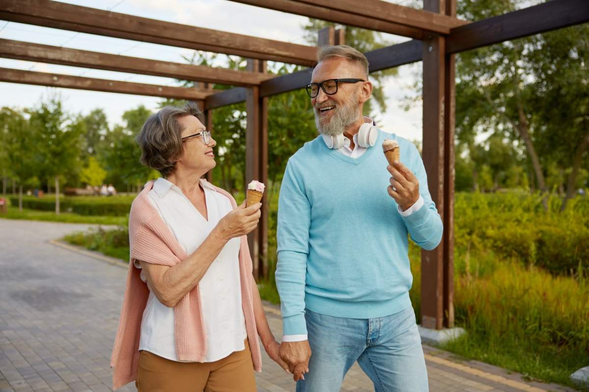Cuplu de seniori vesel care mănâncă cornet de înghețată în parc, bucurându-se de timpul de relaxare