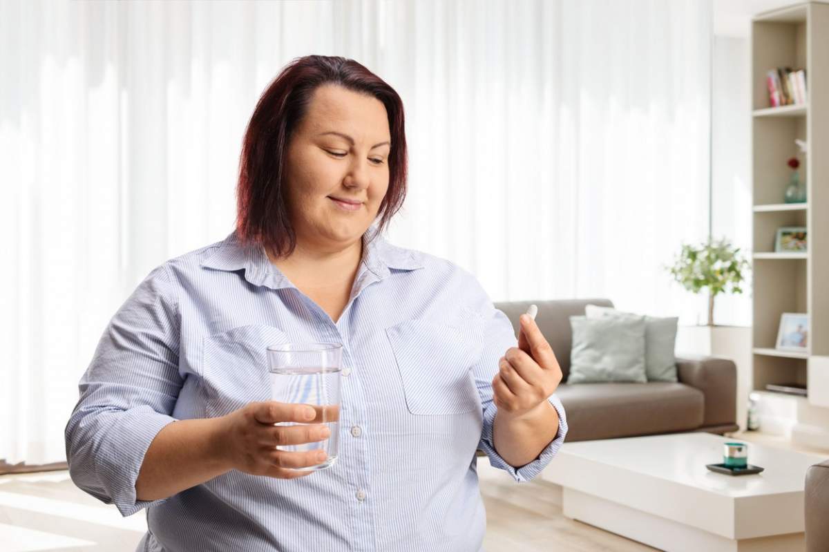 Femeie supraponderală care tine in mana un pahar cu apă și o pastilă