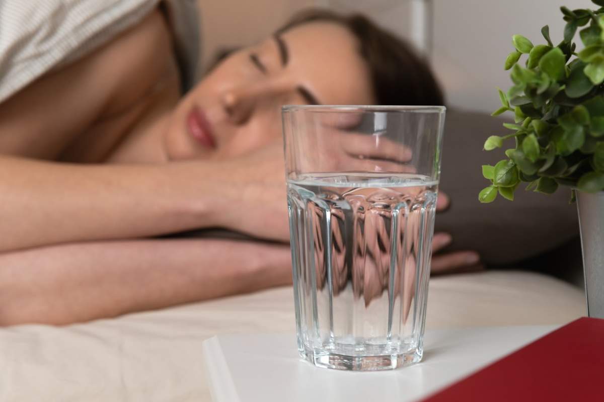 Un pahar de apă lângă un pat în care doarme o femeie