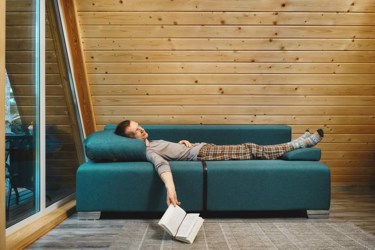 barbat doarme pe canapea cu o carte in mana