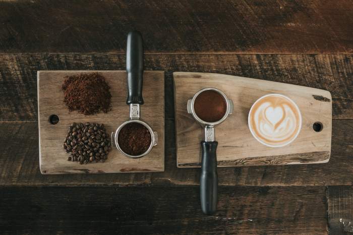 cafea într-o ceașcă și praf de cafea pe două tăvi de lemn.