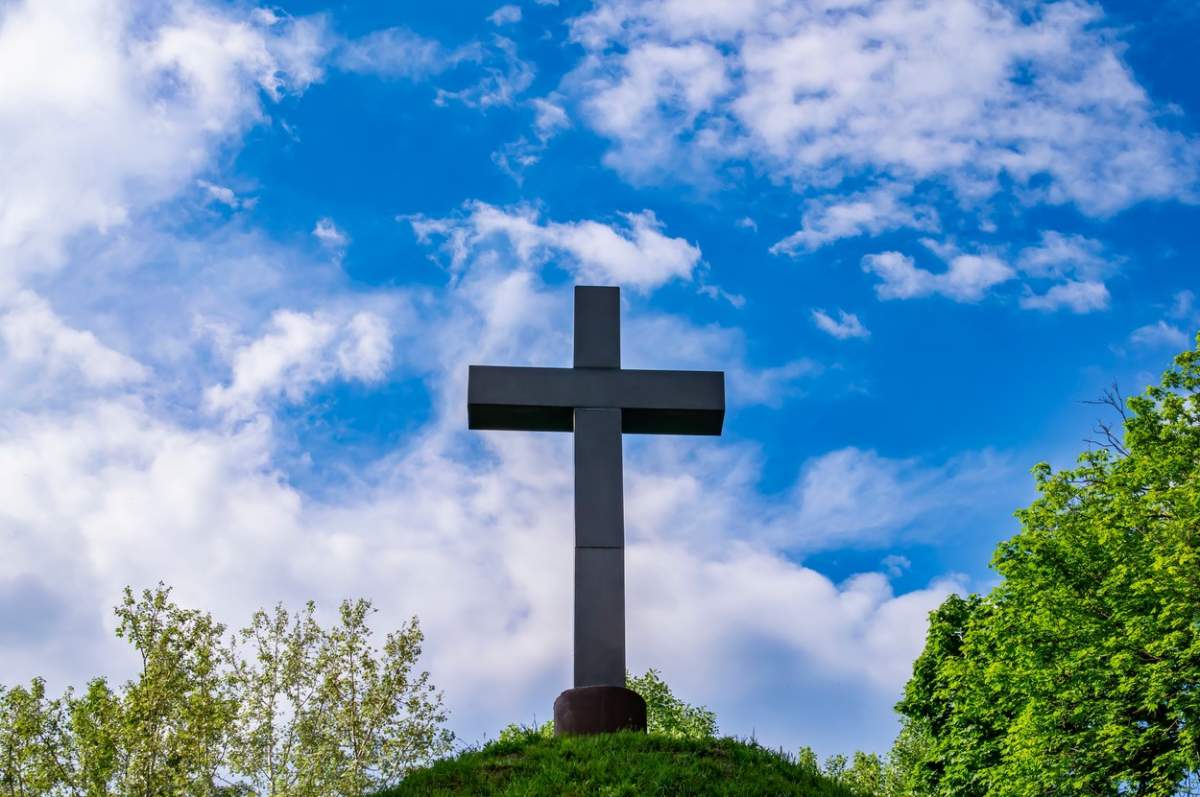 Cruce creștină pe o movilă pe un cer albastru cu nori albi