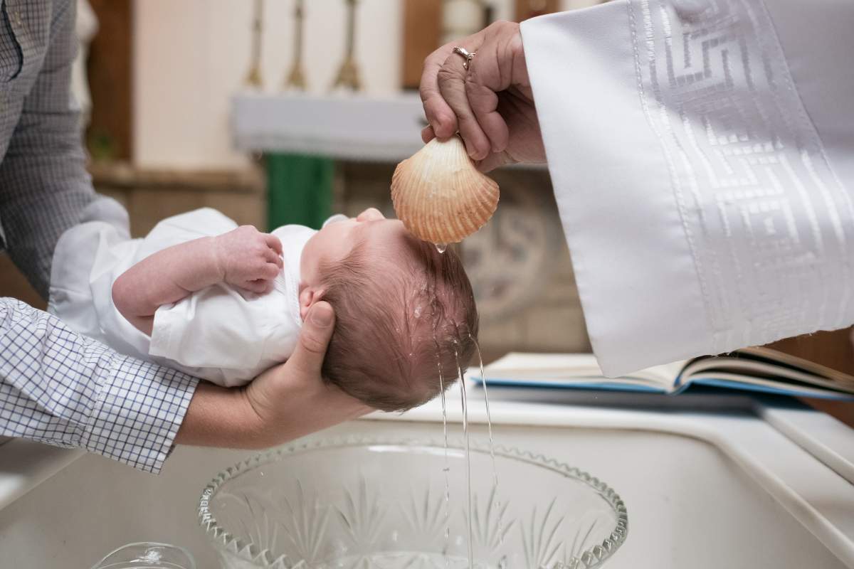 un copil căruia preotul îi toarnă apă pe cap în timpul botezului.