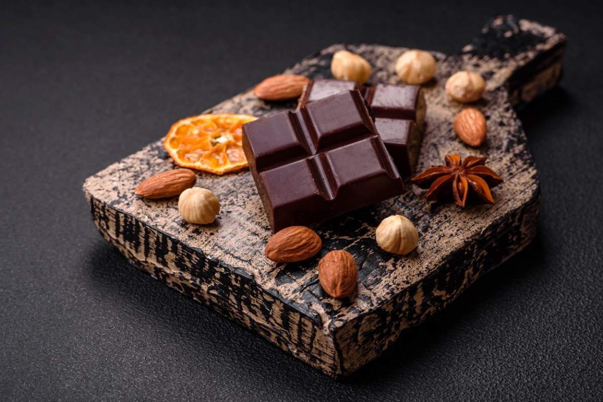 Ciocolată neagră ruptă în cuburi pe un fund din lemn pe un fundal negru