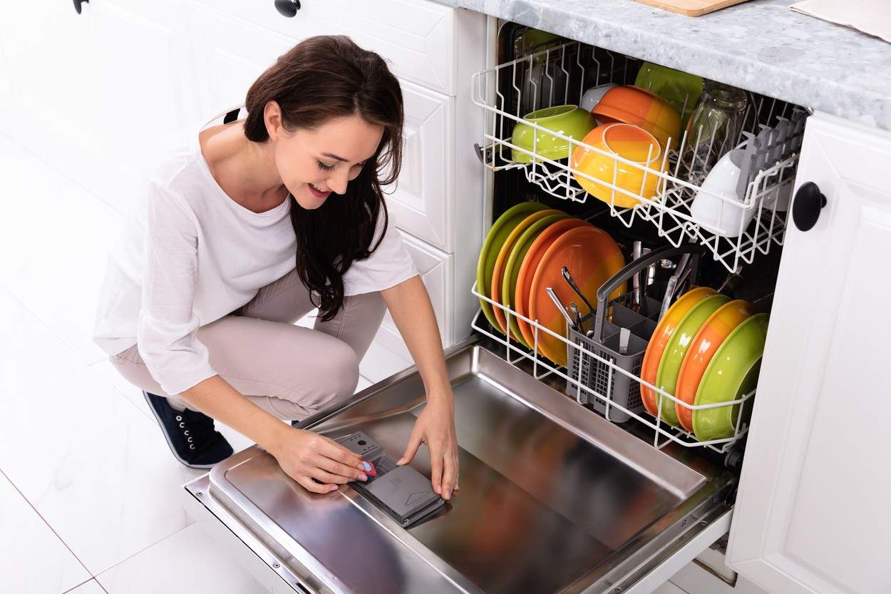 O femeie care pune detergent în mașina de spălat vase