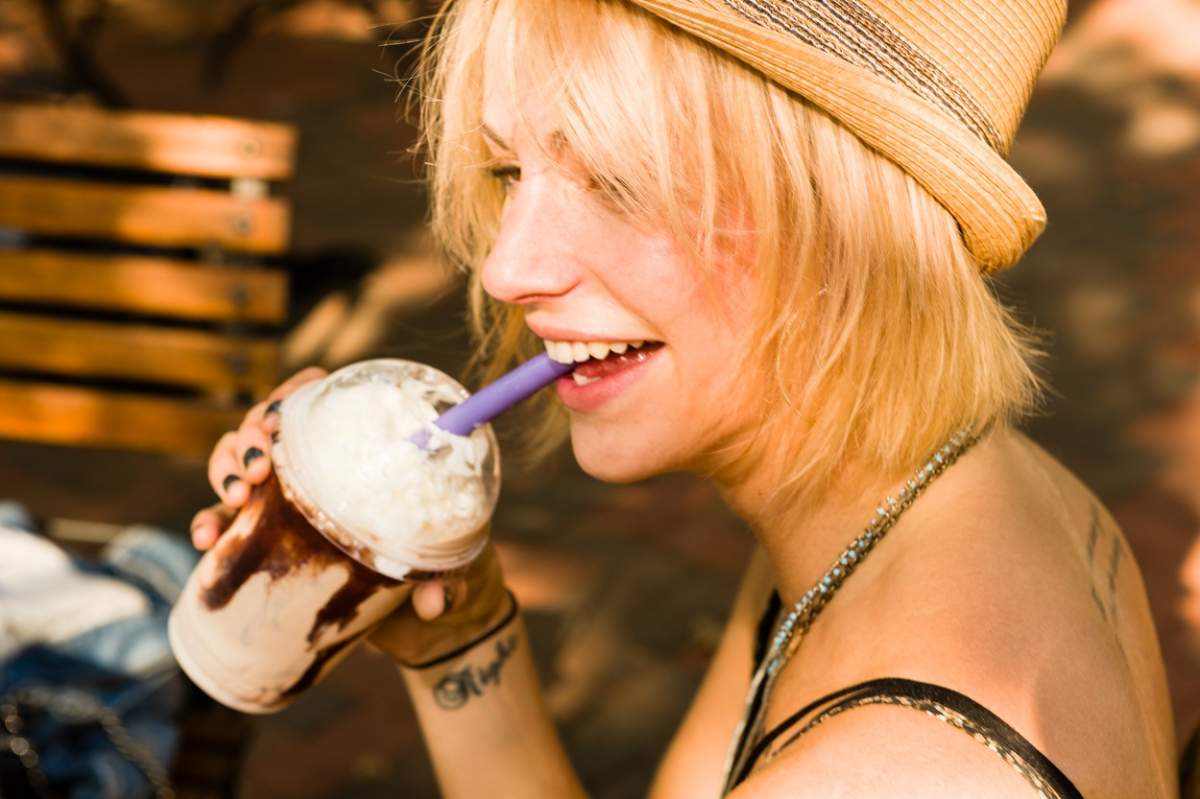 O tânără blondă bea Frappe cu paiul
