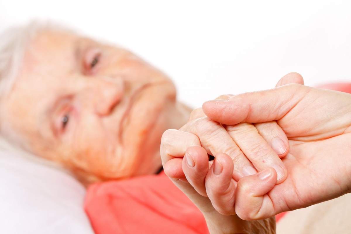 Îngrijitor care ține de mână o pacientă