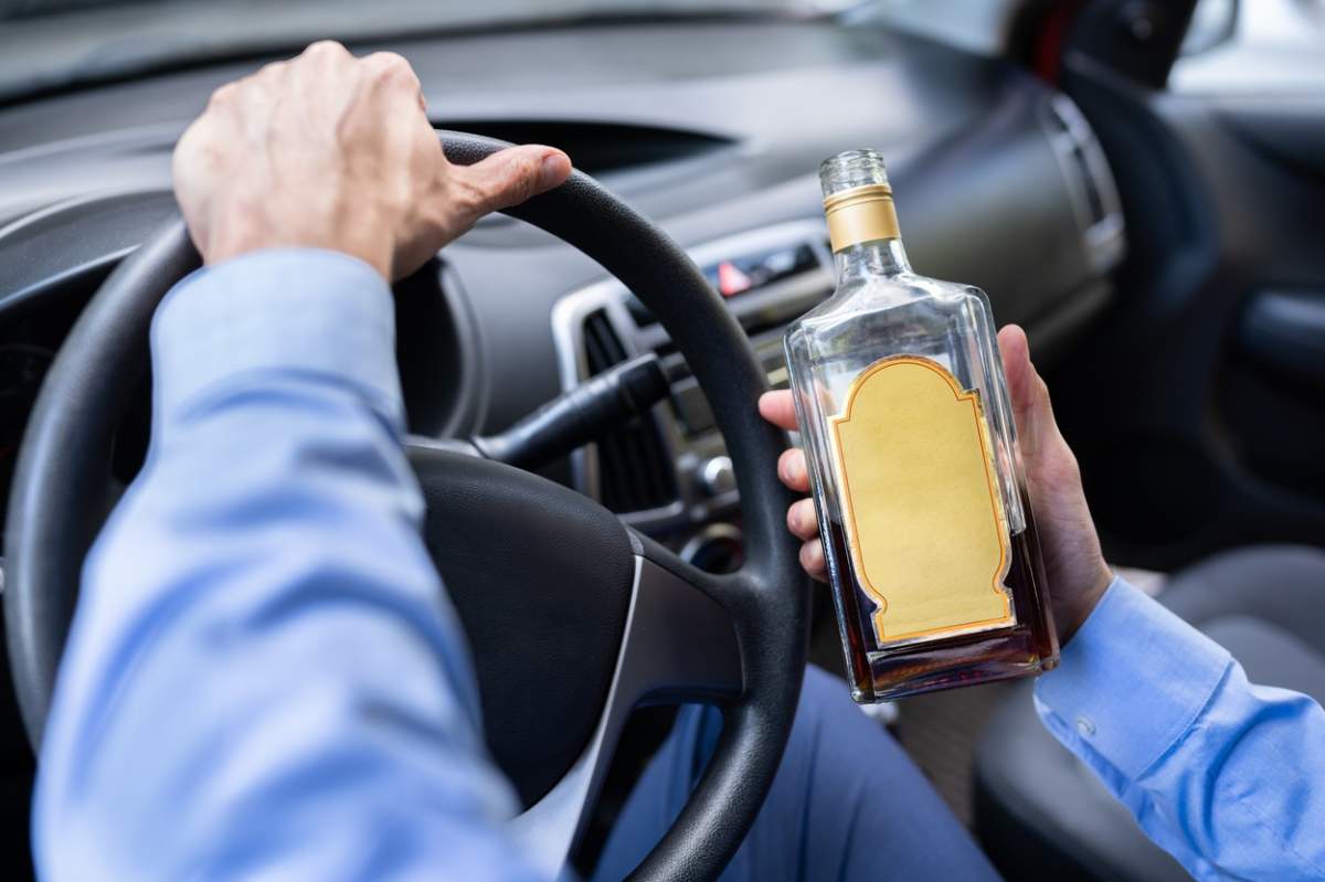 Un șofer conduce cu o sticlă de alcool în mână