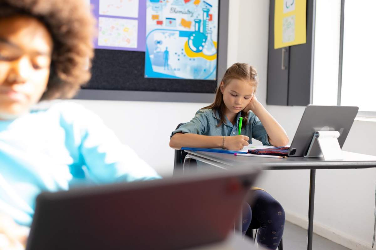 Școlari diverși fericiți stând la birouri în sala de clasă