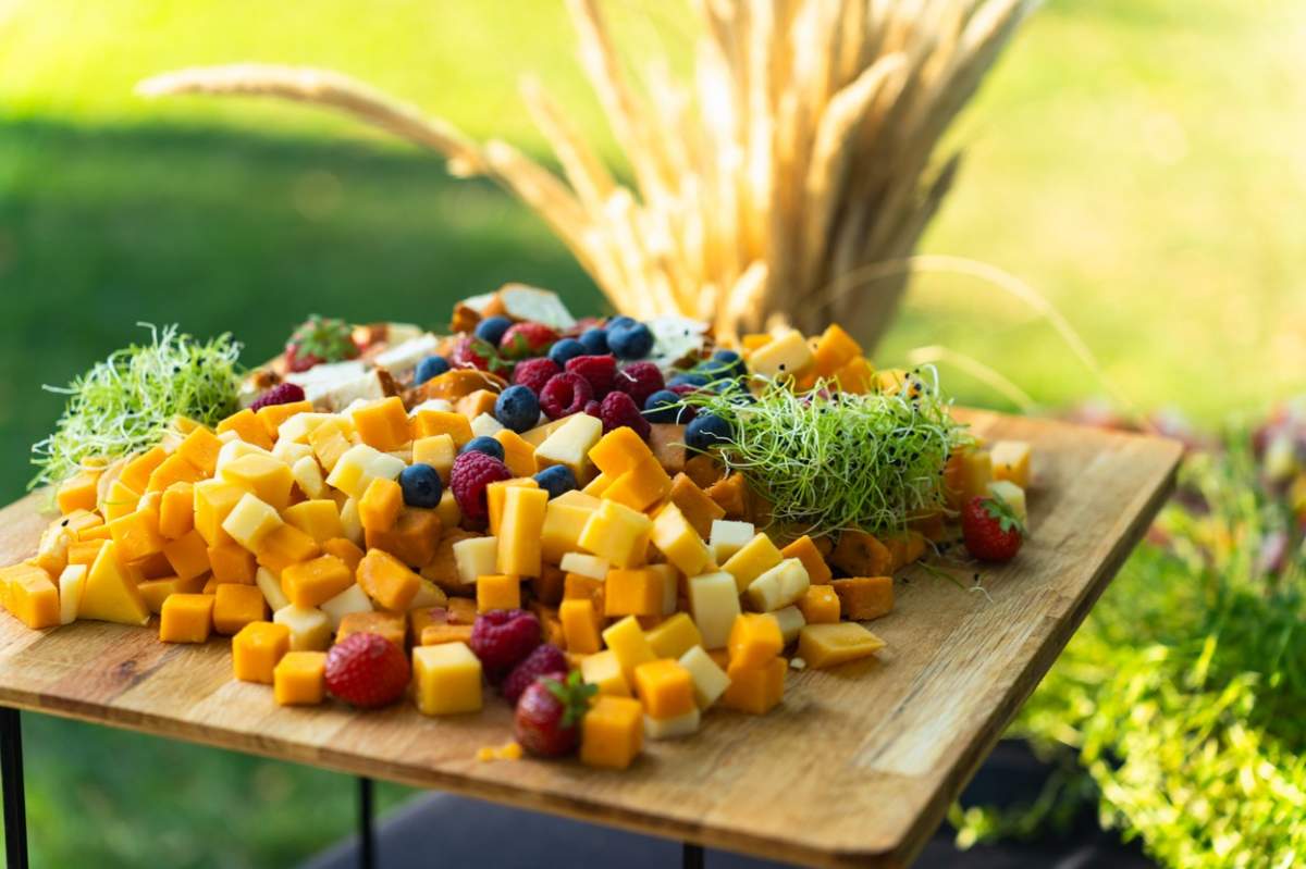 Masă cu diverse tipuri de brânză și fructe pregătite pentru un bufet în curte vara