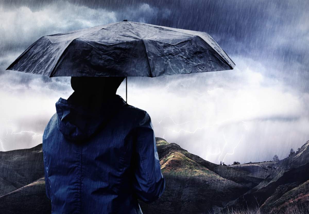 Se pregătește o furtună. Fotografie cu o femeie acoperită cu o umbrelă care urmărește o furtună peste un munte.