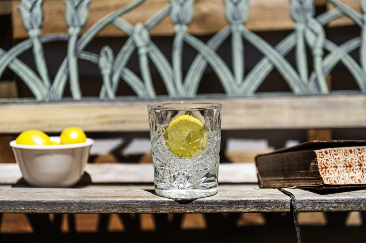 Un pahar de cristal cu apă rece și o felie de lămâie de băut în aer liber pe o bancă de lemn împreună cu o carte de hârtie