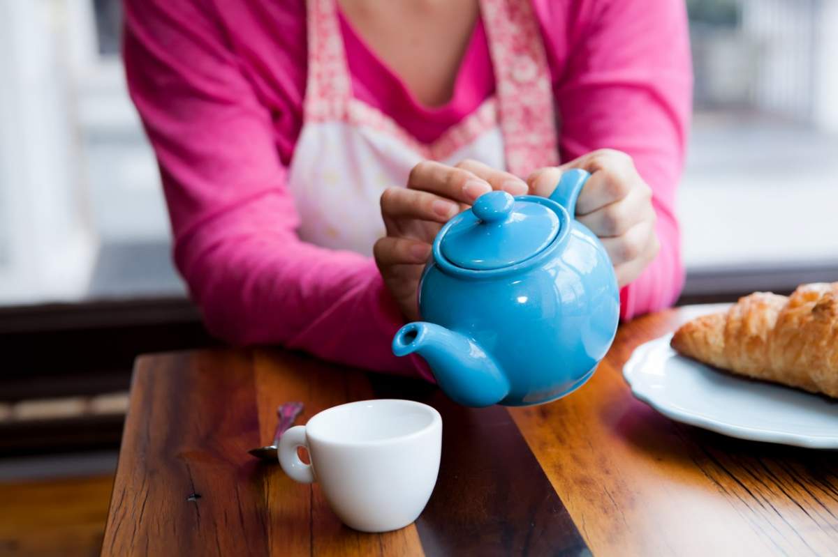 O femei toarnă ceai dintr-un ceainic albastru