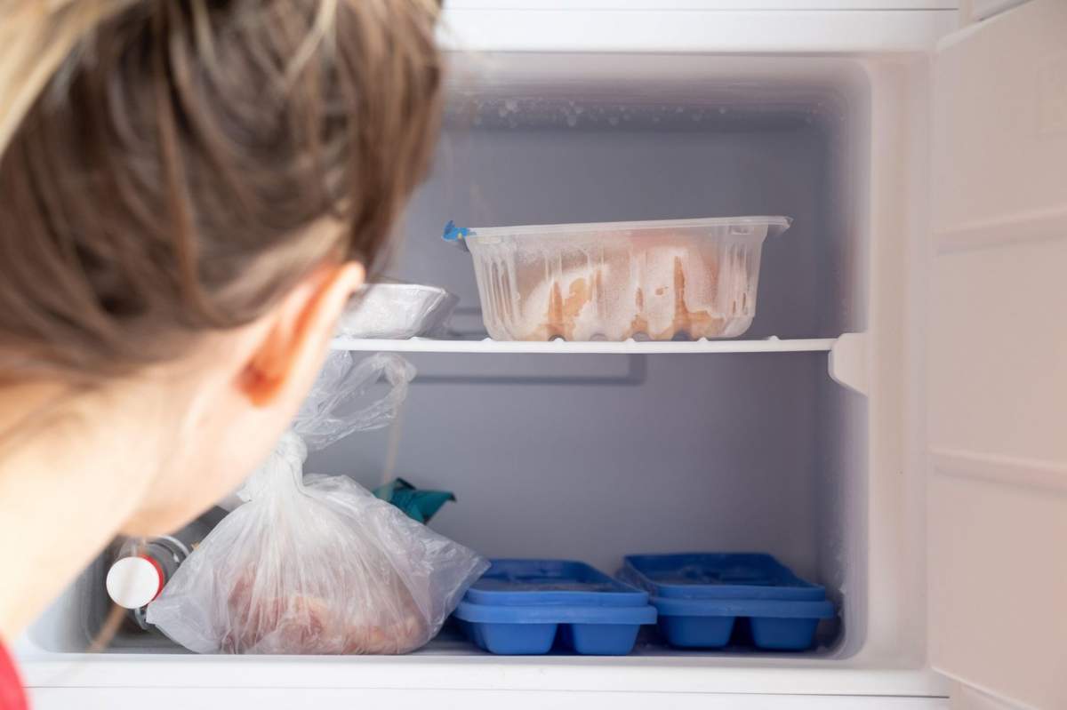 Congelator în frigider, într-o tavă cu gheață și carne și o sticlă de vodcă, mâncare la congelator în bucătărie și fata se uită în frigider