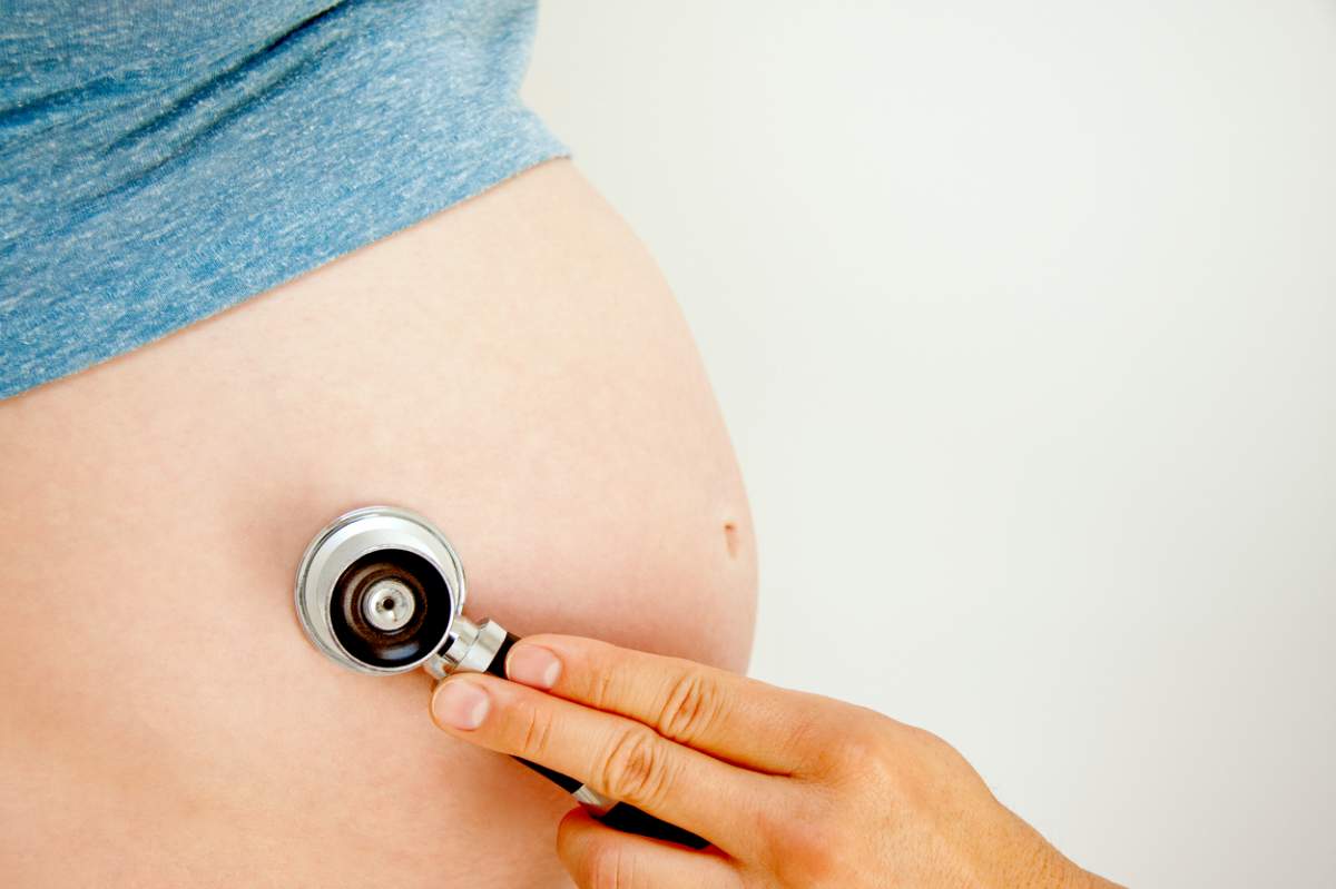 Un medic care ține un stetoscop pe burta unei femei gravide