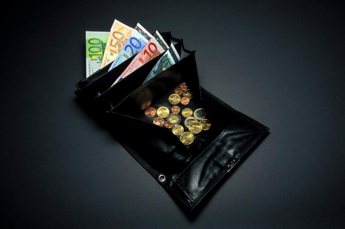 Primul plan al unei poșete sau portofel de chelner negru, monede mici sau libere de euro și cenți, o bancnotă de 5, 10, 20, 50 și 100 de euro este vizibilă