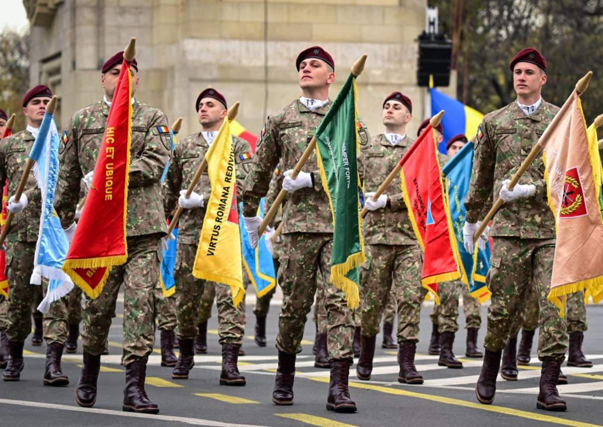 Militarii români afișează diferite steme aparținând Armatei Române în timp ce mărșăluiesc în timpul unei parade militare de marcare a Zilei Naționale a României la București, 1 decembrie 2023