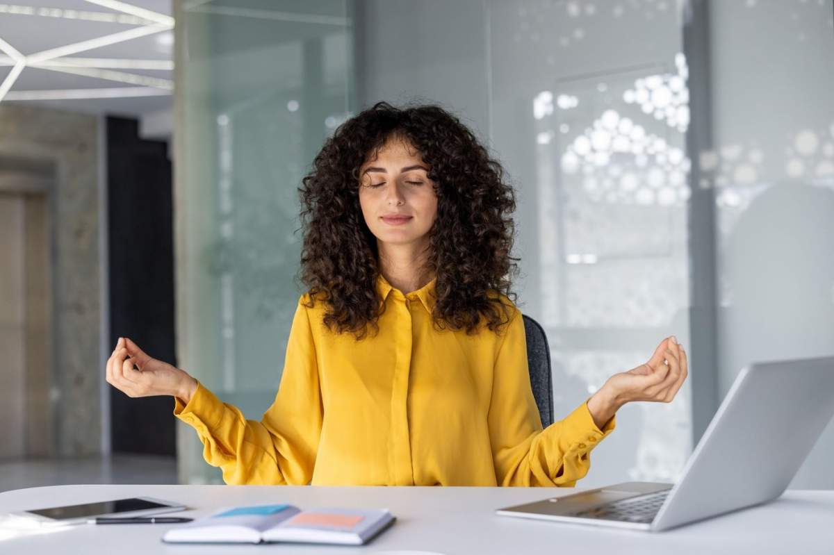 Femeie tânără meditând la biroul de birou cu ochii închiși