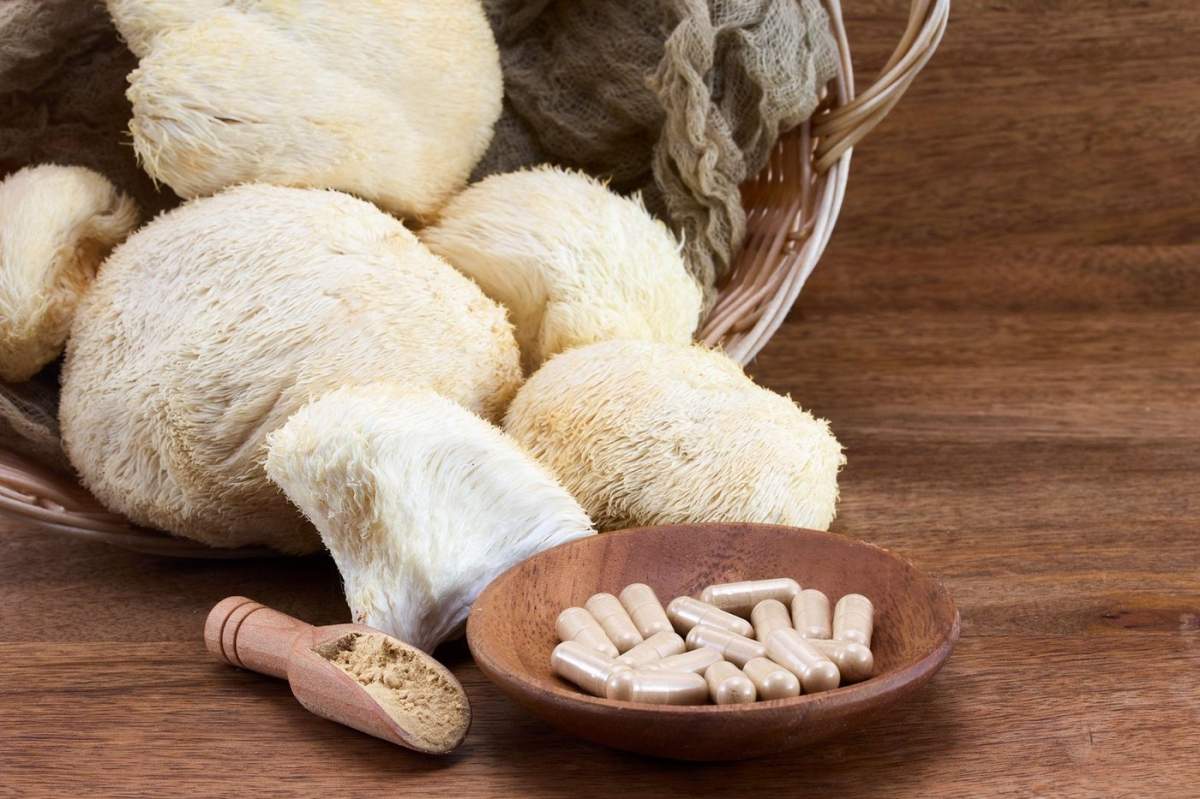 Ciuperci de coamă de leu și capsule de suplimente aranjate pe o suprafață de lemn cu un aspect rustic.