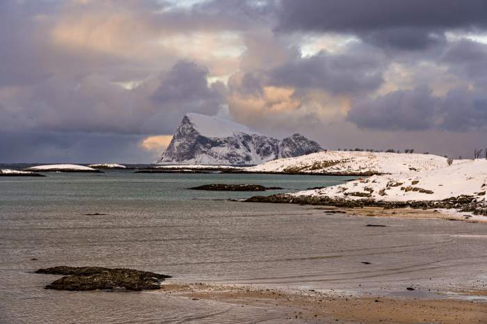 Vedere de pe o plajă de pe insula Sommaroy spre insula stâncoasă Haja iarna, Tromso, Troms, Norvegia, Europa