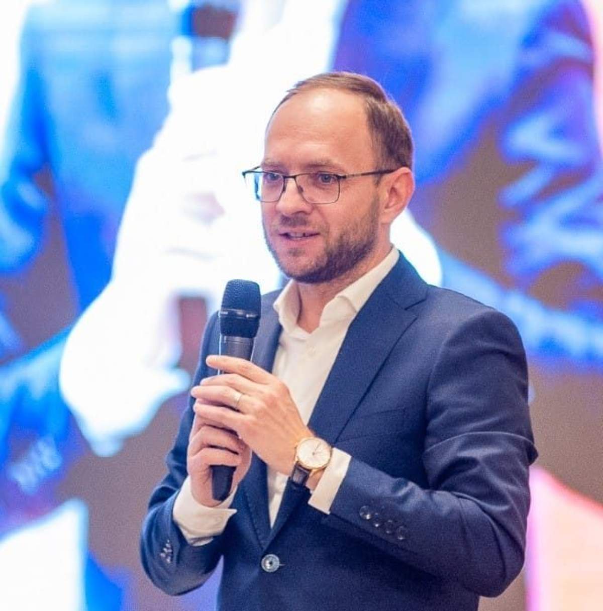 Primarul din Botoșani vorbește la un microfon, cu un ecran în spate Primarul din Botoșani vorbește la un microfon