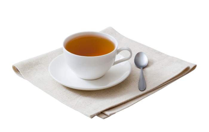 Ceașcă albă de ceai pe un prosop și cu o linguriță