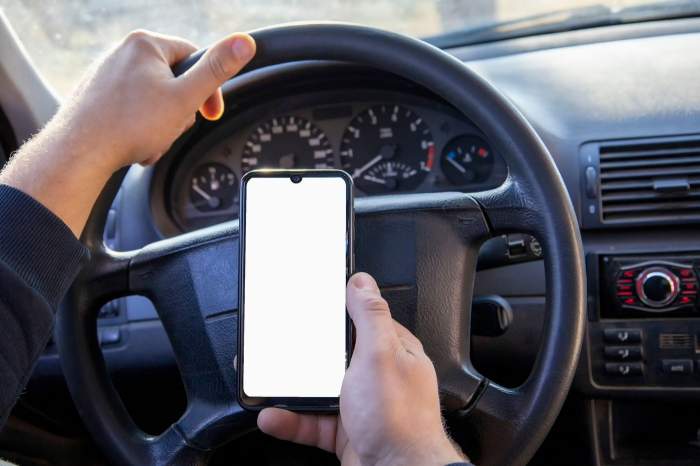 Un bărbat ține un telefon în mână la volan, în mașină