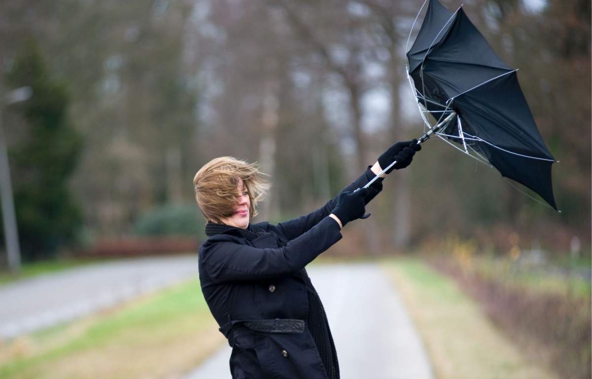 Imagine cu o femeie căreia ii zboară umbrela din cauza vântului