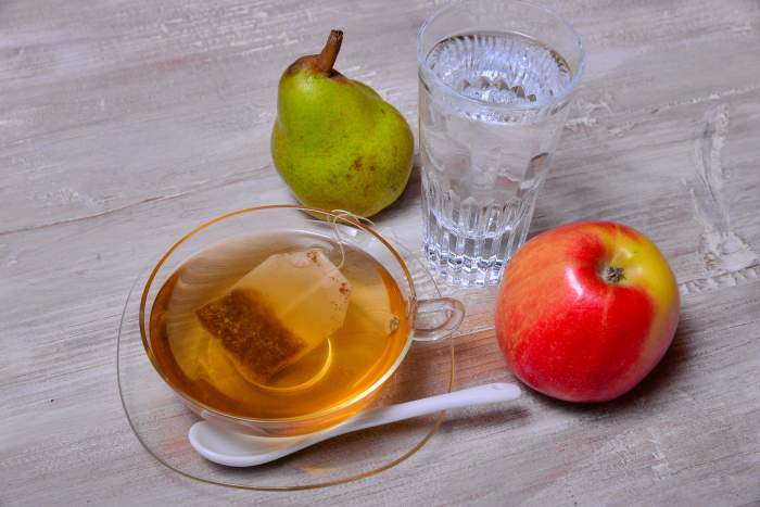 O ceașcă transparentă de ceai cu un măr și o pară