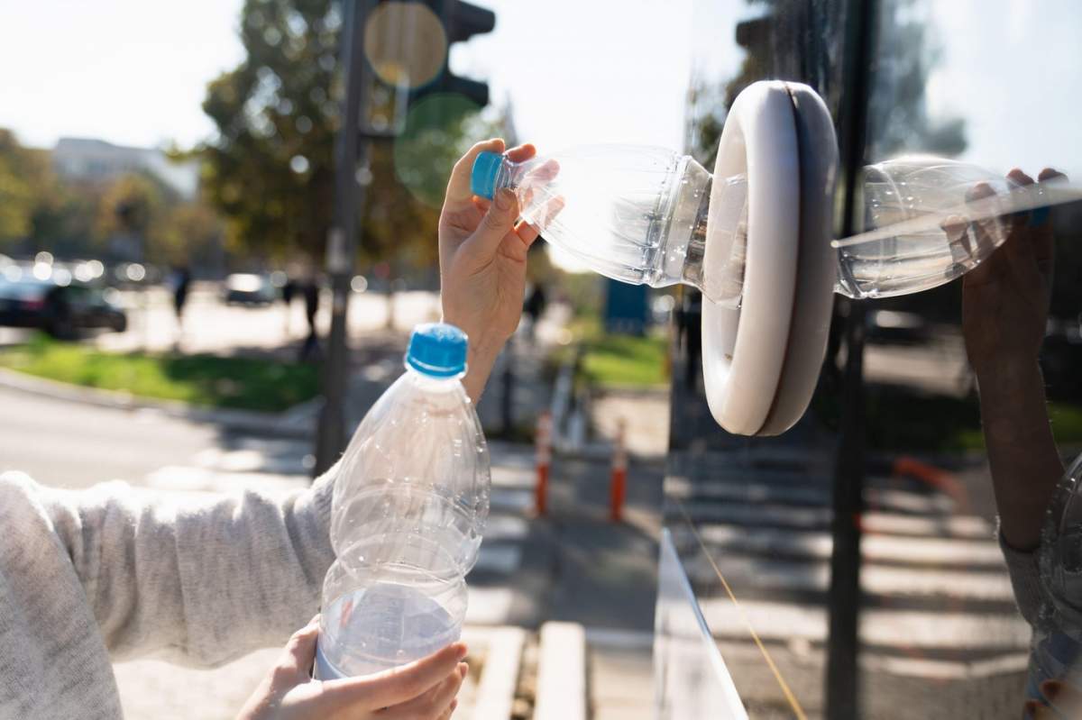 O femeie folosește un aparat cu autoservire pentru a primi sticle de plastic și cutii de conserve uzate pe o stradă din oraș