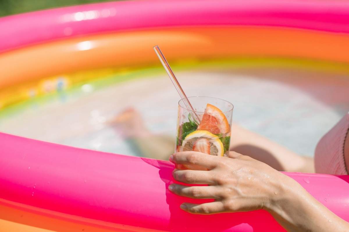 Close-up al unei femei care stă într-o piscină de vară cu o băutură răcoritoare din fructe