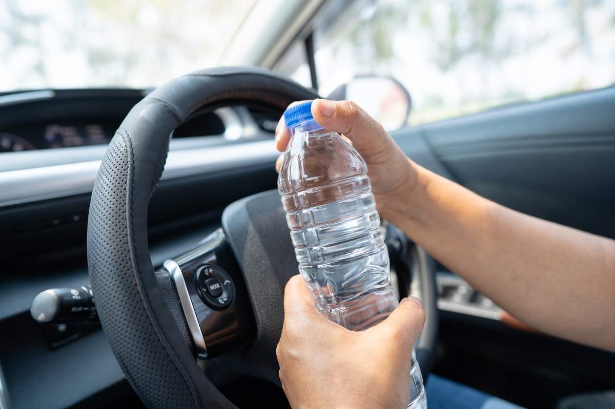 Șofer femeie asiatică care deține sticla pentru a bea apă în timp ce conduce