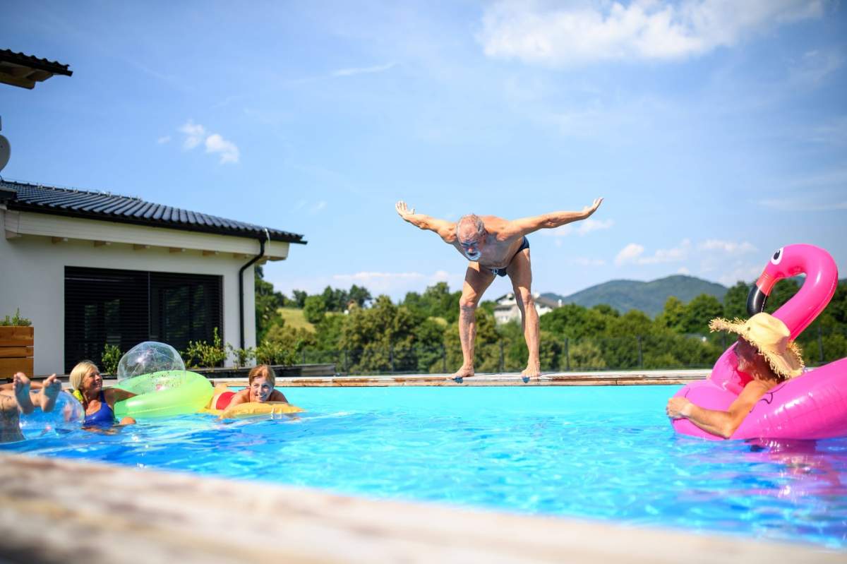 Grup de seniori veseli care se distrează în piscină sărind, înotând