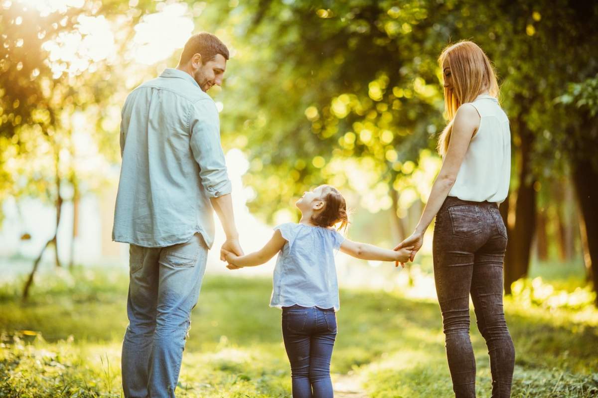 Familie în parc. Mamă, tată și copil plimbare fericită la apus de soare. Conceptul unei familii fericite. Părinții țin copilul de mână.