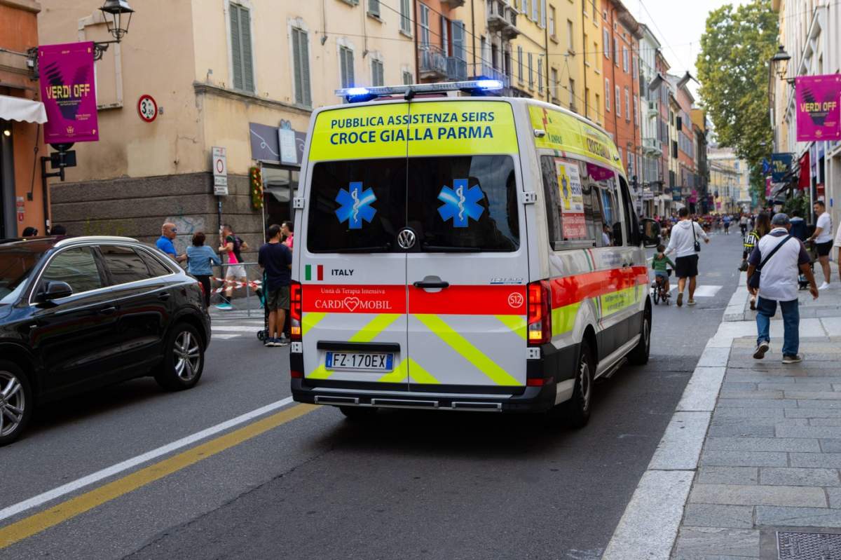 O ambulanță italiană de la Croce Gialla Parma circulând pe o stradă aglomerată din oraș, surprinzând scena dinamică a unui centru urban plin de viață.