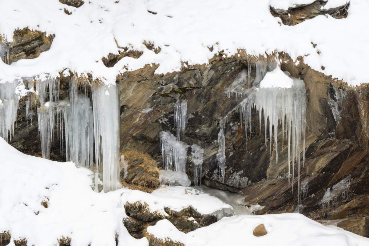 Țurțuri înghețați atârnă de suprafețe stâncoase în mijlocul unui peisaj înzăpezit,