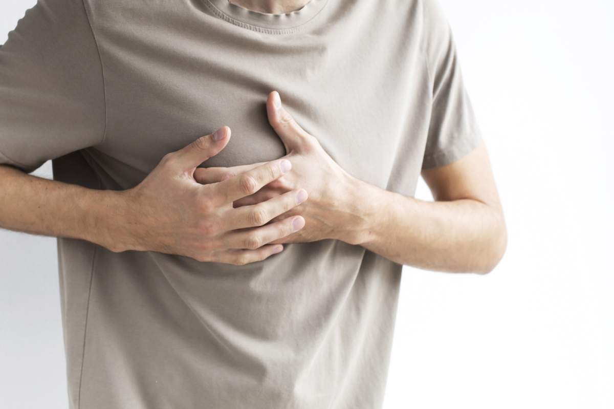 Un bărbat care își strânge mâna în piept de durere, având posibil probleme cardiace, disconfort sau simptome legate de stres, fără chip