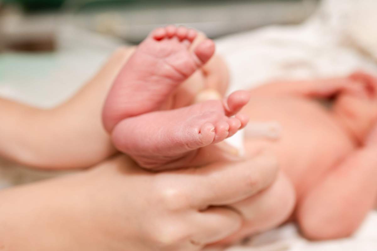 Prim-plan cu picioarele unui nou-născut ținute în brațe de un părinte într-un spital, simbolizând grija, tandrețea și primele momente de viață