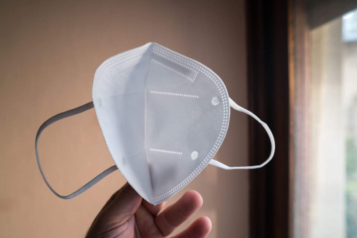 Mână ținând o mască albă FFP2 pe o fereastră pentru prevenirea virusurilor și gripei