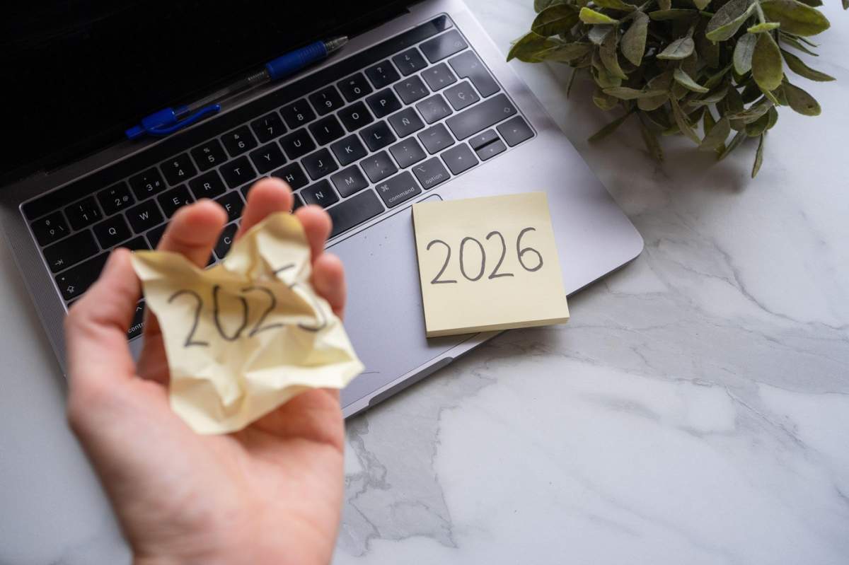 Mâna unei persoane mototolind un bilețel cu 2025, un alt bilețel cu 2026 pe laptop
