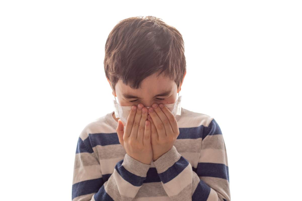 un băiat cu ochii închiși strănută sau tușește în mâini pe fundal alb